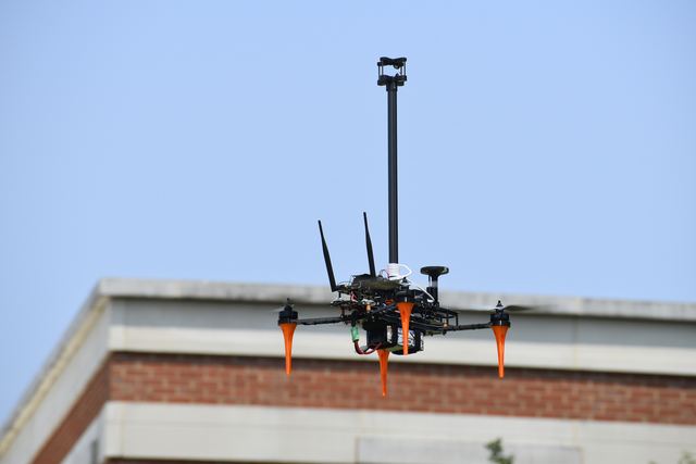 A custom quadrotor with a wind-sensing mast standing on a rooftop parapet.