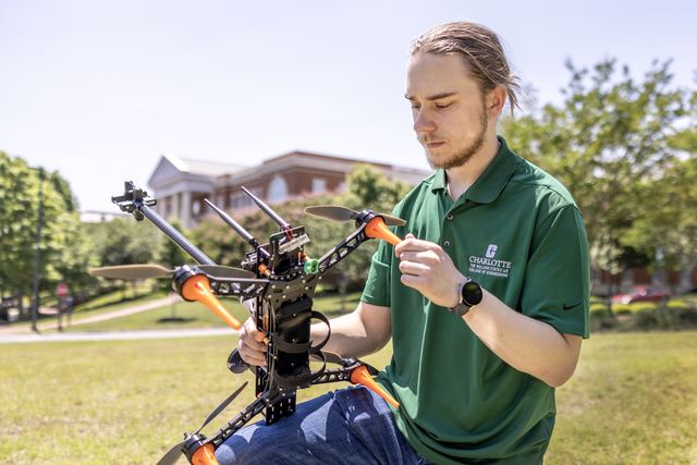 A student seated on a lawn holding a large custom quadrotor fitted with an anemometer mast.