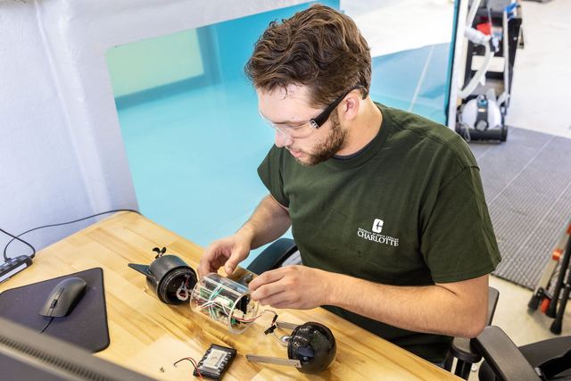 A researcher at a workbench assembling a small wheeled robot and its electronics.