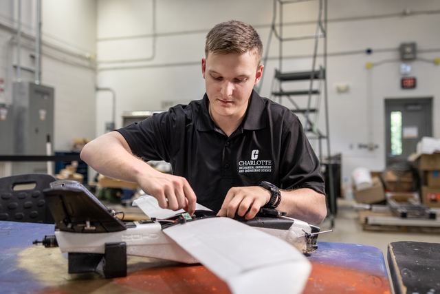 A researcher in the high bay working on a white fixed-wing UAV laid out on a table.