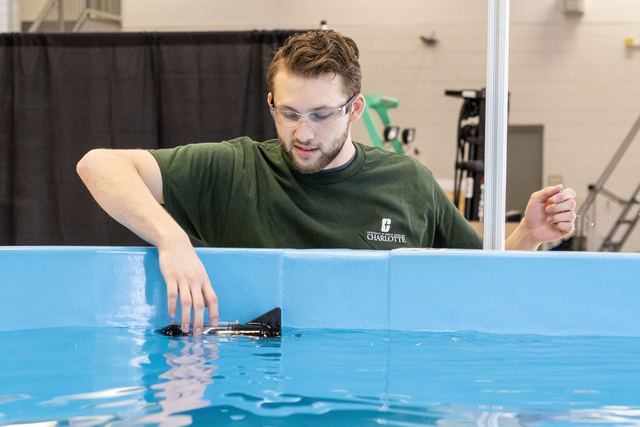 A researcher reaching into the blue-lined water tank to launch a small underwater vehicle.