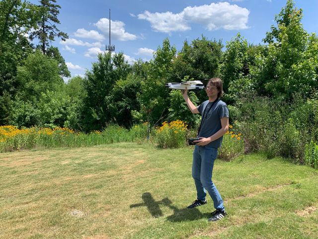 A person standing in a grassy field holding a small quadrotor before launch.