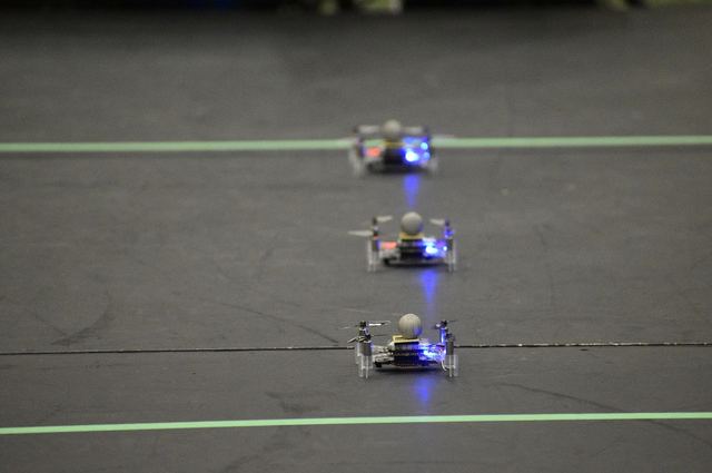 Three small ground robots on a dark test track marked with green lines.