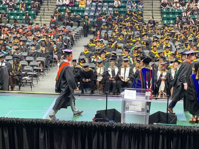 A commencement ceremony in a filled arena, with a graduate crossing the stage.